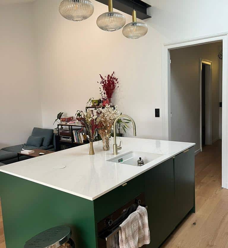 Cuisine îlot vert sapin : design moderne et élégance dorée Cuisine moderne avec îlot central vert sapin, comptoir blanc veiné, robinet doré et trois suspensions. Salon attenant.