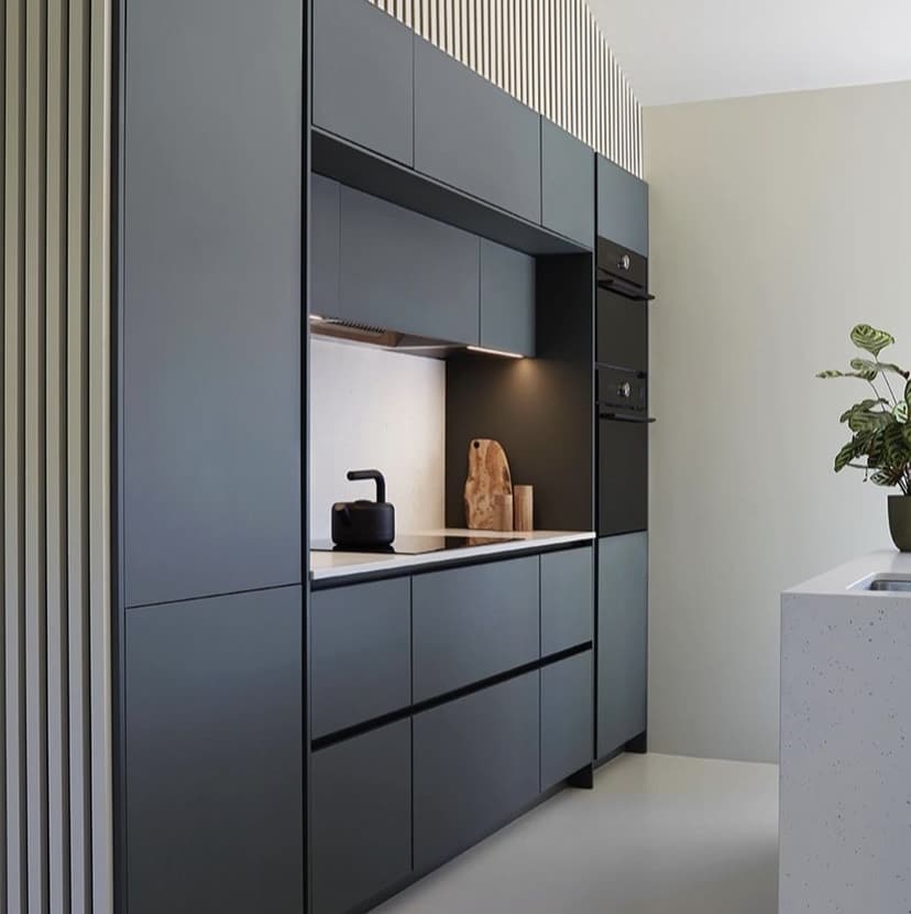 Cuisine Moderne Anthracite | Design Fonctionnel Épuré Cuisine moderne gris anthracite, armoires intégrées, plan de travail clair, plaques induction, bouilloire noire, fours encastrés et mur à lattes.