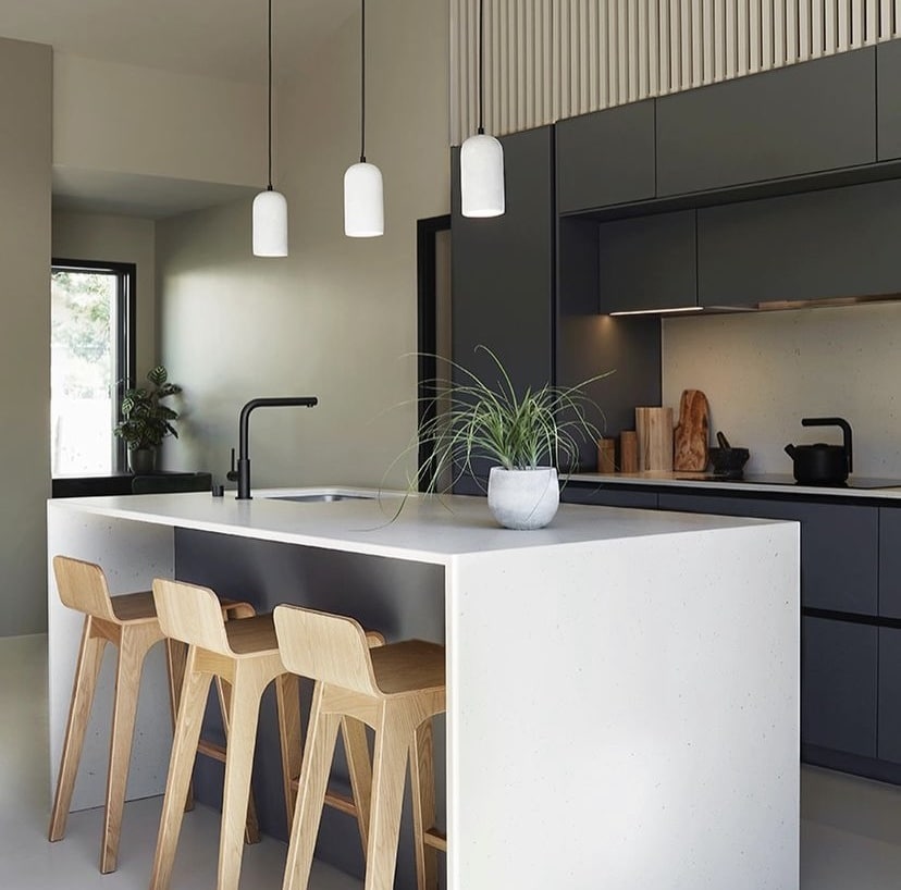 Cuisine moderne : îlot central design et ambiance épurée. Cuisine moderne avec îlot central blanc, trois tabourets en bois clair. Armoires sombres, robinet noir et luminaires suspendus minimalistes.