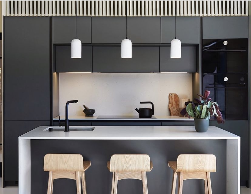 Cuisine moderne grise, îlot central blanc avec évier, 3 tabourets bois clair. Fours encastrés, 3 suspensions blanches. Design épuré.